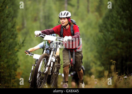 group of athlete mountainbikers climb a step uphill in forest during Regional competitions on cross-country bike Stock Photo