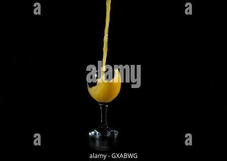 jet orange juice being poured into a glass beaker on a black background Stock Photo