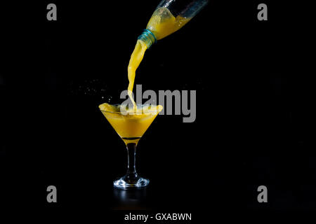 orange juice is being poured into a glass beaker from a bottle on black background Stock Photo