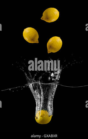 Lemons are falling into the water holding up a lot of splashes on a dark background Stock Photo
