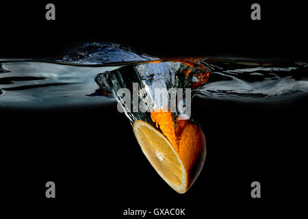 Orange in water raised a big wave on a dark background Stock Photo