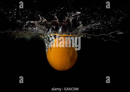 Orange in water raised a big wave on a dark background Stock Photo