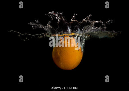 Orange in water raised a big wave on a dark background Stock Photo
