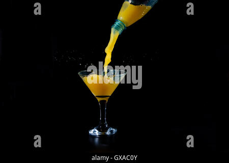 orange juice is poured from a plastic bottle into a glass beaker on a black background Stock Photo