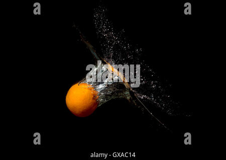 Orange in water raised a wave on a dark background Stock Photo