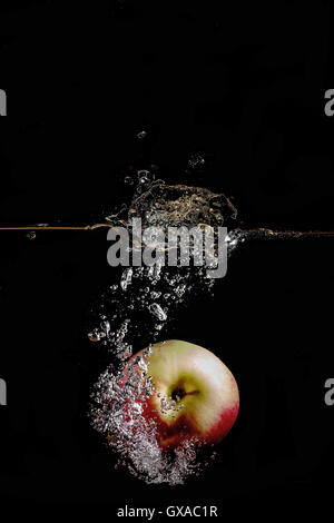 red apple fell into the water and climb up many splashes on black background Stock Photo