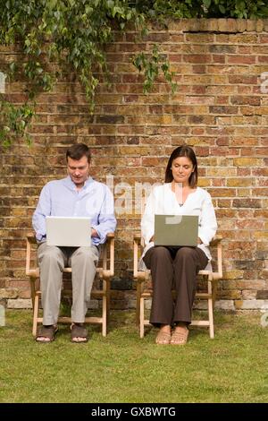 Mature couple sitting in garden using laptops Stock Photo