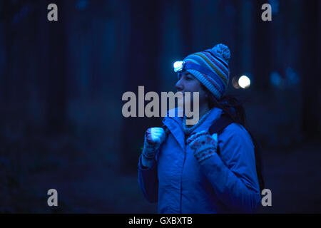 Female hiker wearing head torch hiking through forest at night Stock Photo