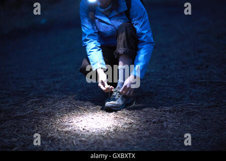 Female hiker wearing head torch tying hiking boot laces at night Stock Photo