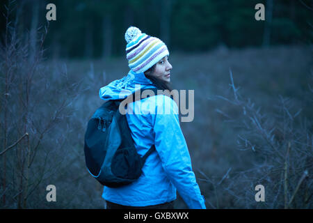 Female hiker looking back whilst hiking in forest at dusk Stock Photo