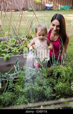 Mother and daughter in garden, watering plants together with hose Stock Photo