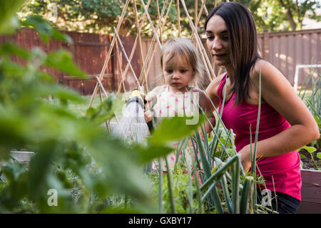 Mother and daughter in garden, watering plants together with hose Stock Photo