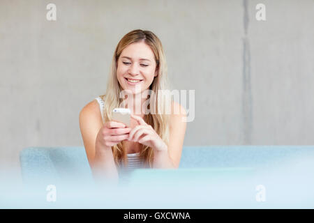 Young female student sitting on study space sofa using smartphone at higher education college Stock Photo