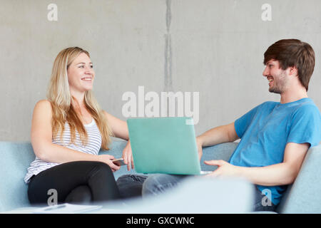 Young male and female students sitting on study space sofa using laptop at higher education college Stock Photo