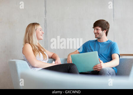 Young male and female students sitting on study space sofa with laptop at higher education college Stock Photo