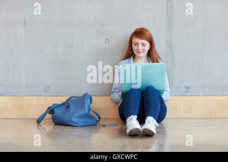 Young female student sitting on floor using laptop at higher education college Stock Photo
