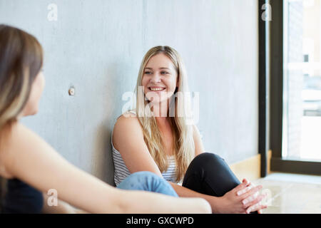 Two young female students sitting on floor chatting at higher education college Stock Photo