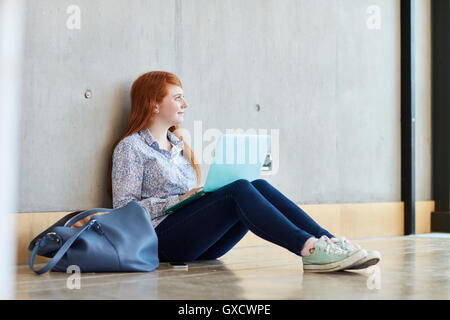 Young female student sitting on floor with laptop at higher education college Stock Photo