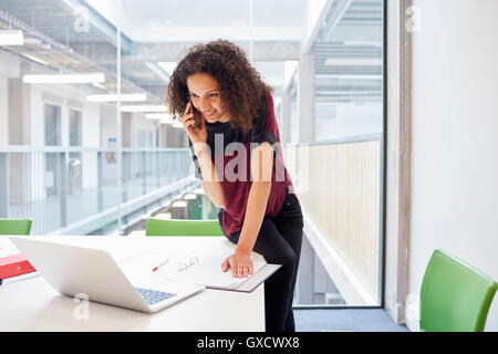 Female designer reading laptop and talking on smartphone  in design studio Stock Photo