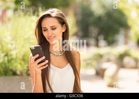Young businesswoman reading smartphone text in city Stock Photo