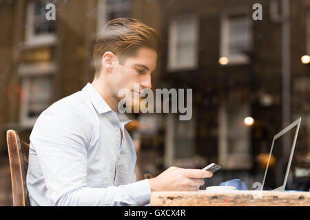 Window view of young businessman reading smartphone texts in cafe Stock Photo