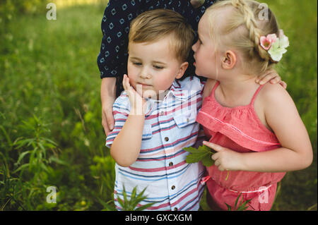 Girl whispering in brothers ear in meadow Stock Photo