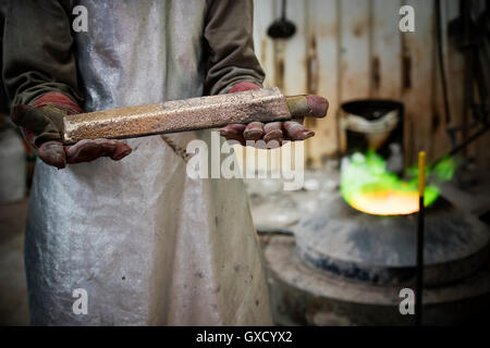 Mid section of male foundry worker holding bronze ingot in bronze foundry Stock Photo