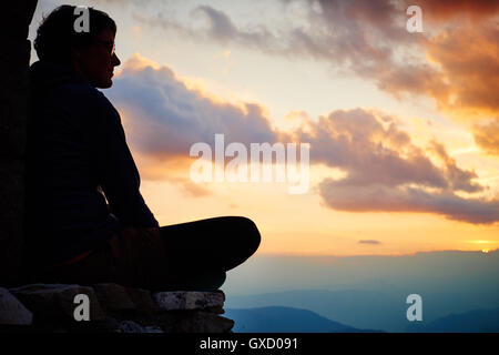 Silhouette of woman sitting cross legged watching sunset Stock Photo