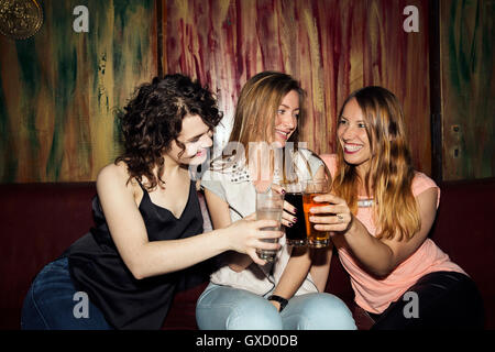Three adult female friends raising a glass whilst sitting in bar Stock Photo