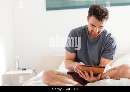 Man sitting on bed using digital tablet Stock Photo
