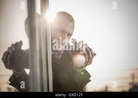 Man in business attire behind corner at harbour poised with handgun, Cagliari, Sardinia, Italy Stock Photo