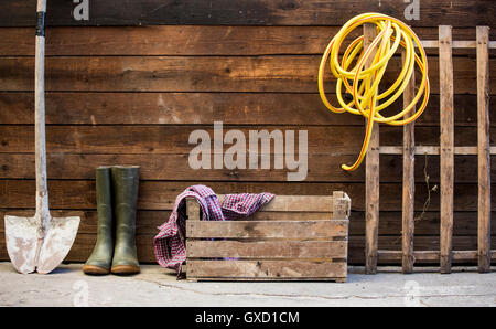 Row of spade, rubber boots and hosepipe by shed Stock Photo