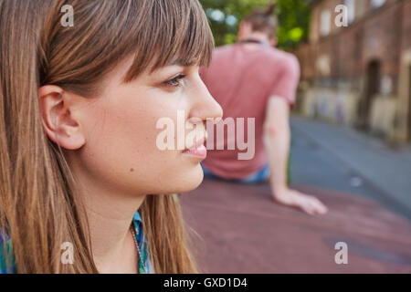 Young couple outdoors, sitting away from each other, sad expression on young woman's face Stock Photo