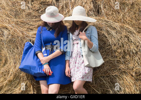 Two females wearing sun hats, leaning against hay, faces hidden Stock Photo
