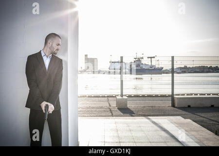 Man in business attire behind wall at harbour poised with handgun, Cagliari, Sardinia, Italy Stock Photo