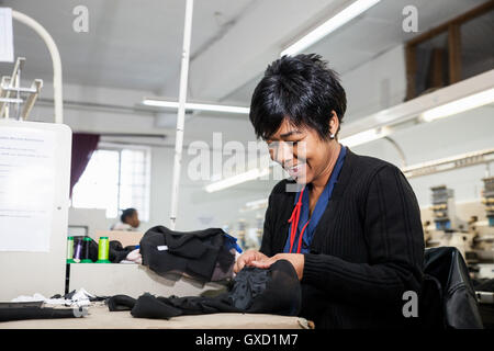 Female factory worker removing stitches from black cloth from speed stitching programmed embroidery machine in clothing factory Stock Photo