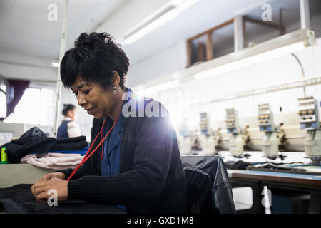 Female factory worker removing stitches from black cloth from speed stitching programmed embroidery machine in clothing factory Stock Photo