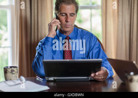 Mature man at home, using laptop and smartphone Stock Photo