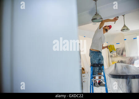 Man up stepladder painting ceiling Stock Photo