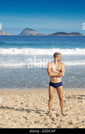 Mature man standing on beach, Ipanema, Cagarras islands, Rio de Janeiro, Brazil Stock Photo