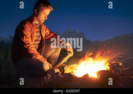 Man crouching by campfire at night, Jackson, Wyoming, USA Stock Photo