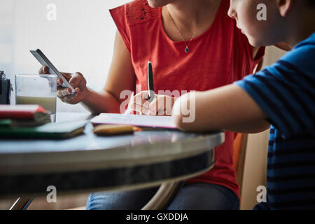 Mother at dining table helping son with homework Stock Photo
