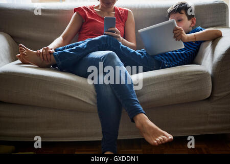 Mother and son relaxing on sofa using digital tablet and smartphone Stock Photo