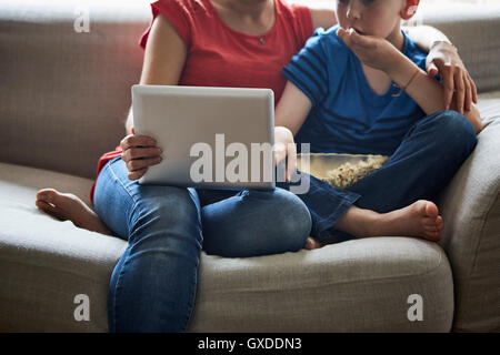 Cropped view of mother and son on sofa with popcorn using smartphone Stock Photo