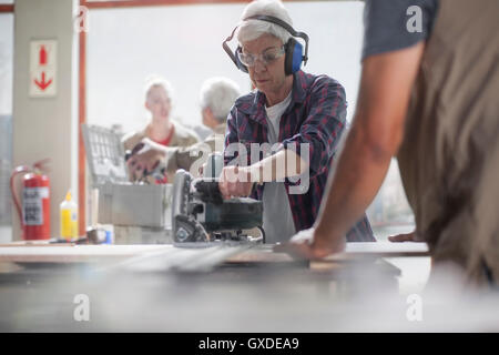 Senior female carpenter using power saw in furniture making workshop Stock Photo