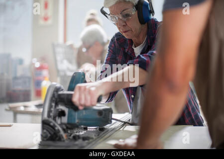 Senior female carpenter using power saw in furniture making workshop Stock Photo