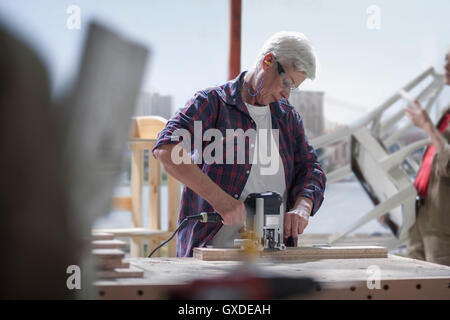 Mature female carpenter using sander in furniture making workshop Stock Photo