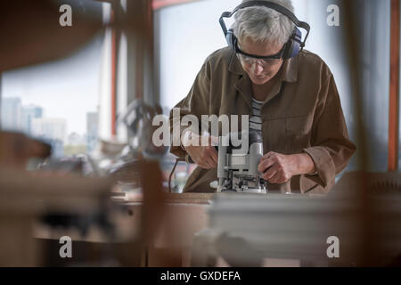 Mature female carpenter using sander in furniture making workshop Stock Photo