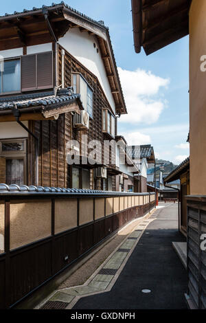 Japan, Izushi. Narrow path between housing, typical Japanese large timber and plaster housees found in semi-rural areas. Traditional style wall. Stock Photo