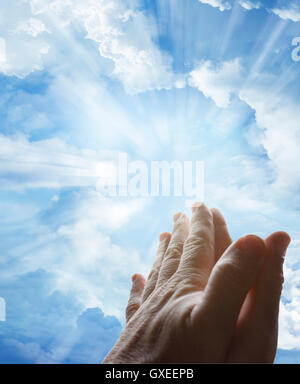 Hands together praying in bright sky Stock Photo